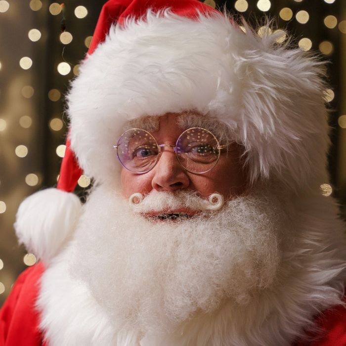 Close-up of a smiling Santa Claus with round glasses and curly mustache.