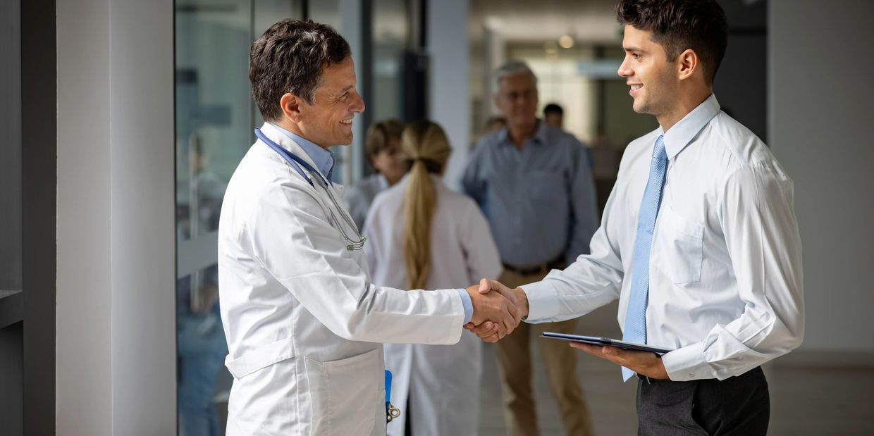 Doctor and businessman shaking hands in a hospital corridor, smiling.