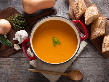 A bowl of pumpkin soup with bread on the side.