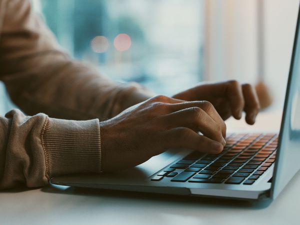 Person typing on a laptop keyboard near a window with natural light.