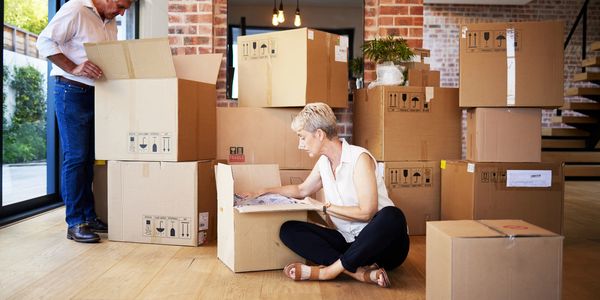 Couple unpacking boxes in a new home with wooden floor and brick walls.
