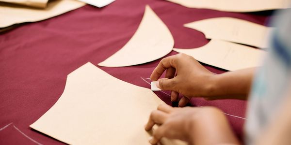 Hands marking fabric with pattern pieces for sewing.