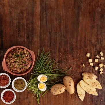 Ingredients for a rustic meal including potatoes, boiled eggs, spices, and herbs on a wooden surface.