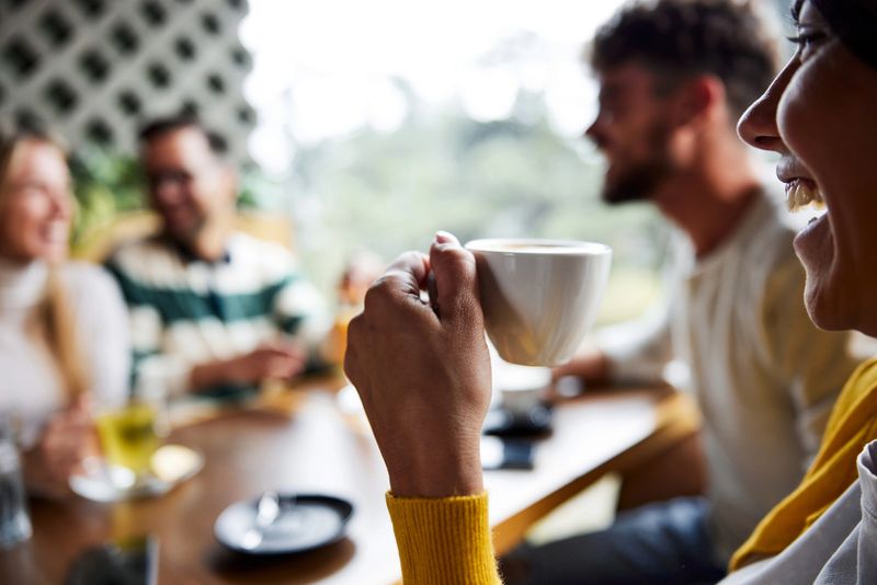 Close up of happy woman drinking coffee while talking to her friends in a cafe.