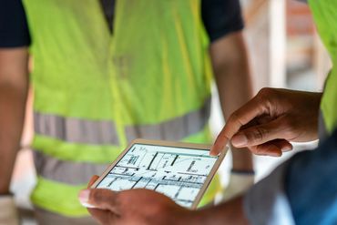 Construction workers reviewing blueprints on a tablet at a site.