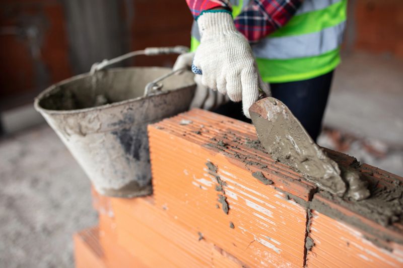 Close-up of a hand of a mason worker putting mortar on bricks. Cropped shot of a bricklayer building a wall at construction site.