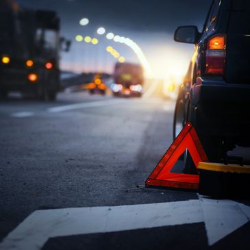Broken down car with warning triangle on road at dusk.