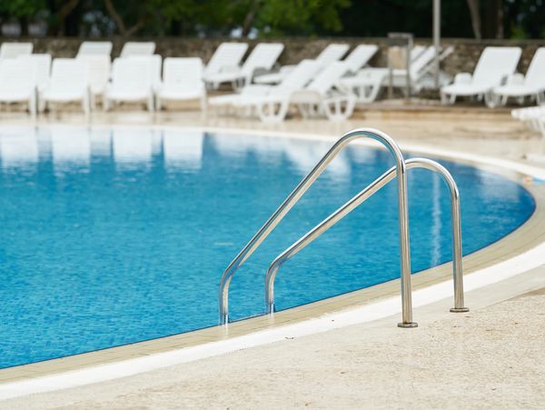 Empty pool with metal handrails and white lounge chairs around it.