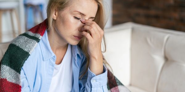 A woman wrapped in a blanket looks stressed and tired, pinching the bridge of her nose.