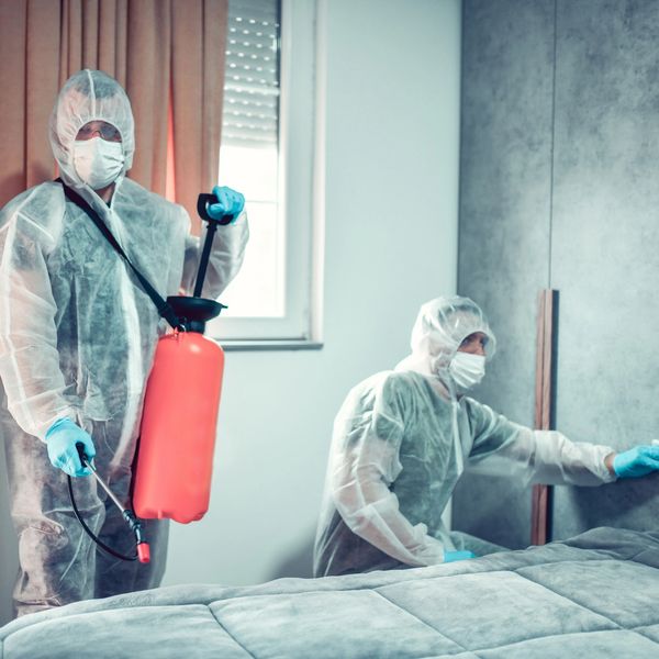 Two people in protective suits disinfecting a room.