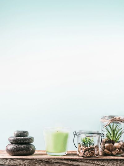 Zen stones, candle, and plants in jars on wooden surface.