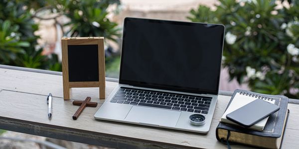Workspace with laptop, wooden cross, and notebook.