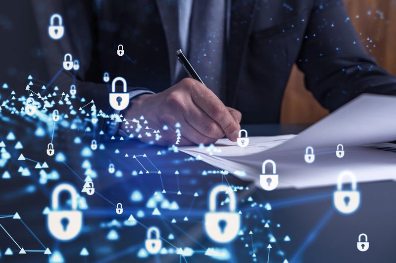 A businessman in formal wear signing the contract to prevent probability of risks in cyber security. Padlock Hologram icons over the working desk.