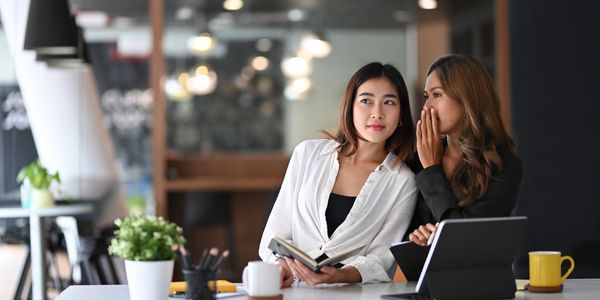 Two women sharing a secret in a modern office setting.