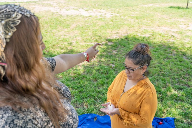 Kneeling woman praying with a candle in her hands while another woman sprays her
