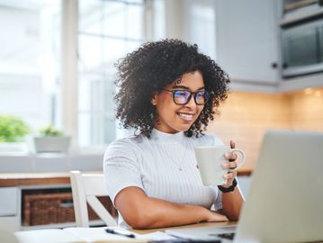 Woman smiling while looking at laptop with coffee.