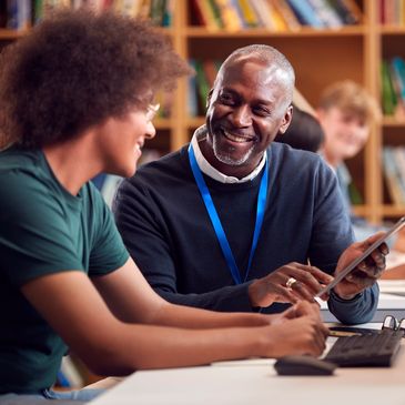 Teacher assisting student with tablet in a library setting.