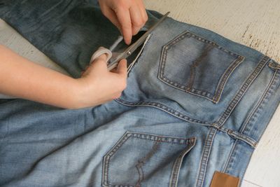 Person cutting a pair of blue jeans with scissors.