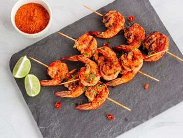 Grilled shrimp skewers seasoned with spices and garnished with lime and chili.