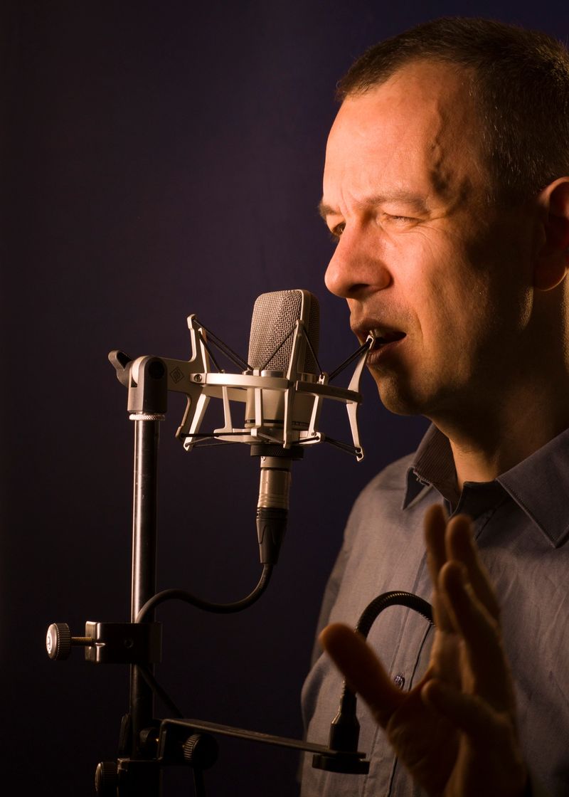 Voiceover artist voice actor in vocal recording studio with larg diaphragm microphone and antipop shield.
