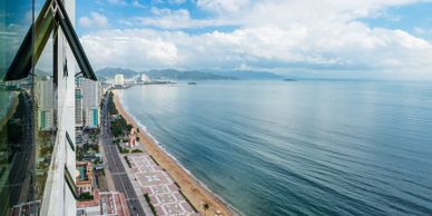 A coastal cityscape with a beach and calm sea under a partly cloudy sky.