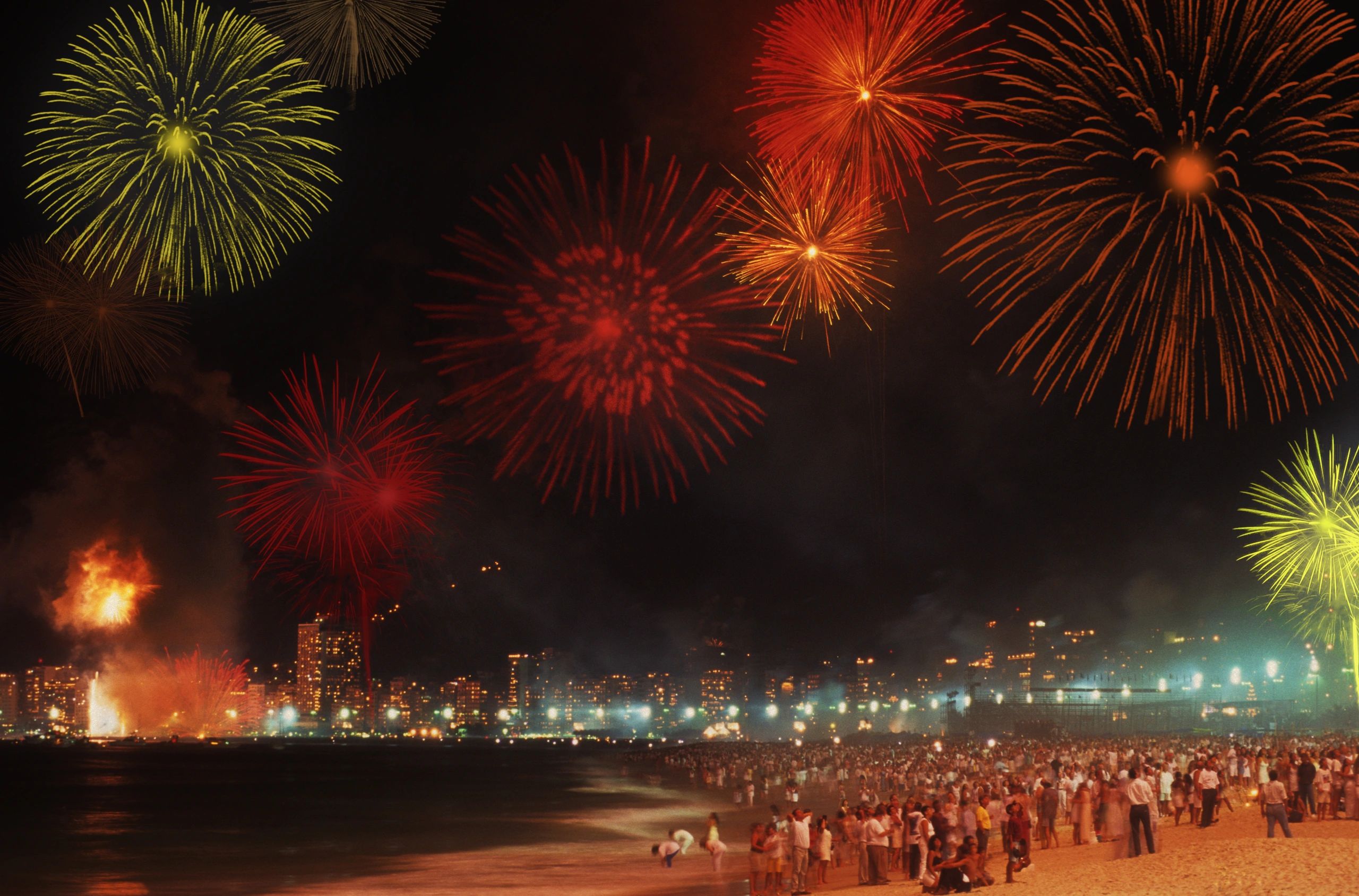 Fogos de artifício coloridos à noite em uma praia cheia de pessoas.