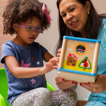 Image of a Hispanic female therapist and a young African-American girl playing with a toy