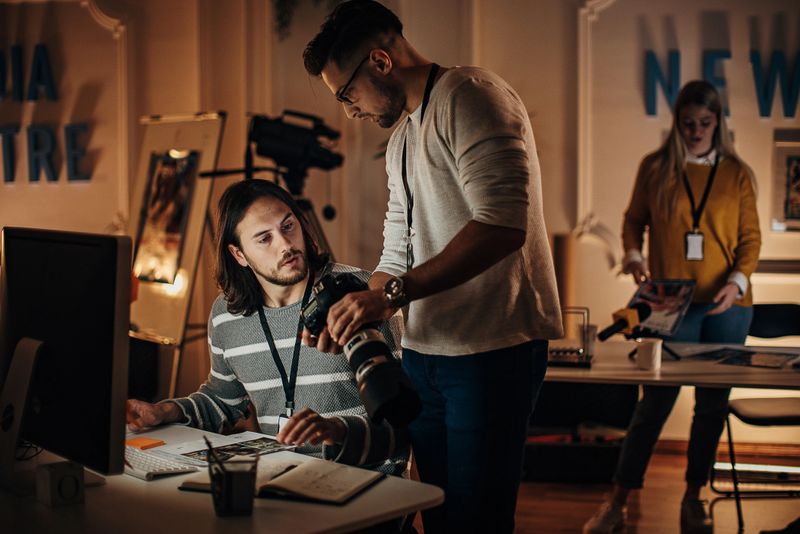 Group of people, male and female journalists working together in news editorial office at night.