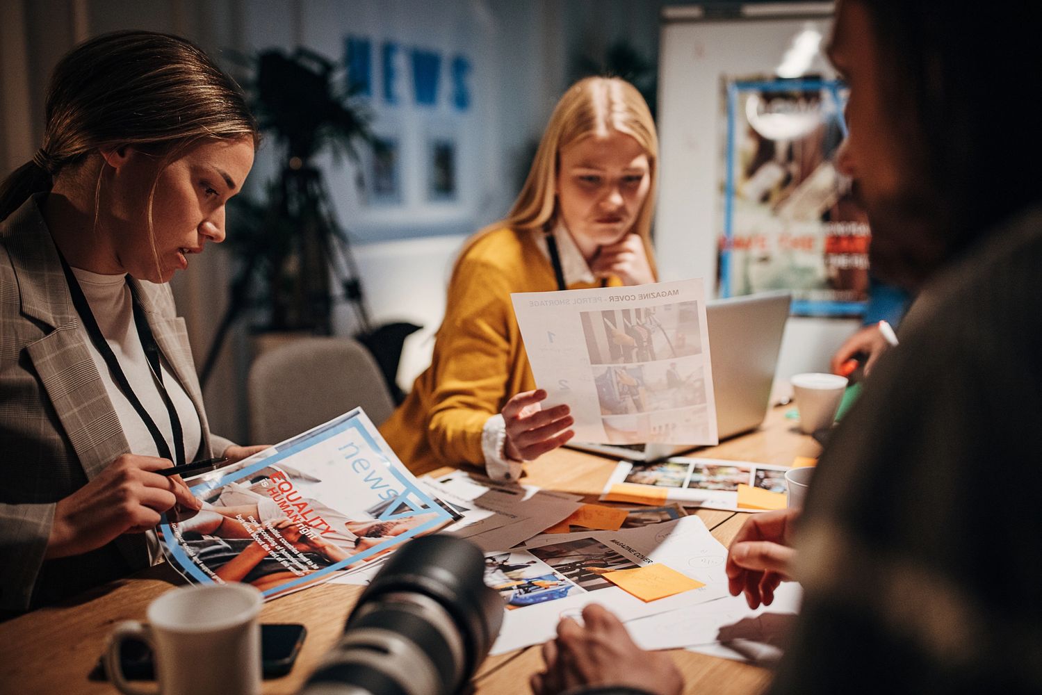 Three individuals reviewing magazine and news layouts at a worktable.