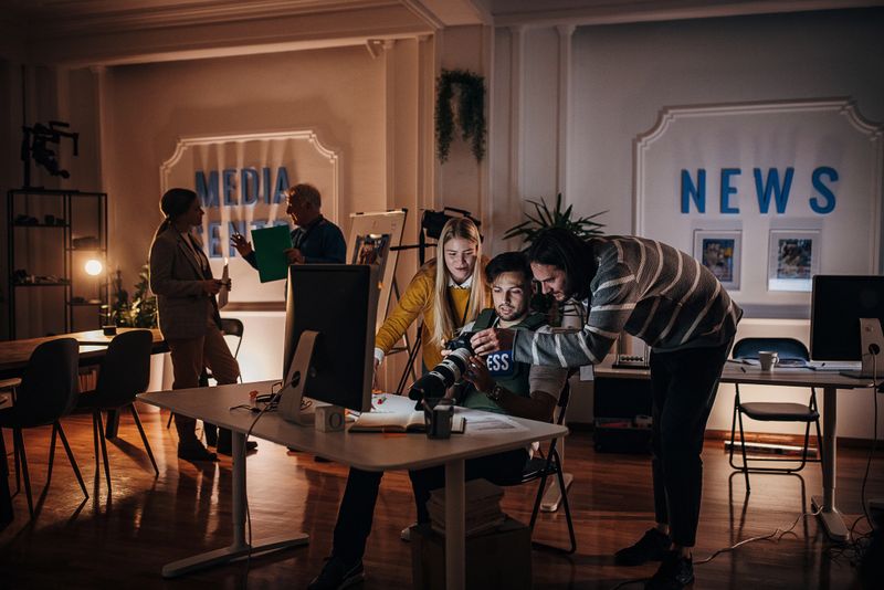 Group of people, male and female journalists working together in news editorial office at night.