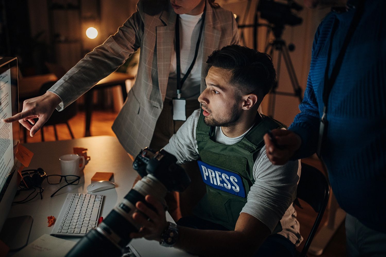 Photojournalists in a dimly lit room reviewing content on a computer screen.