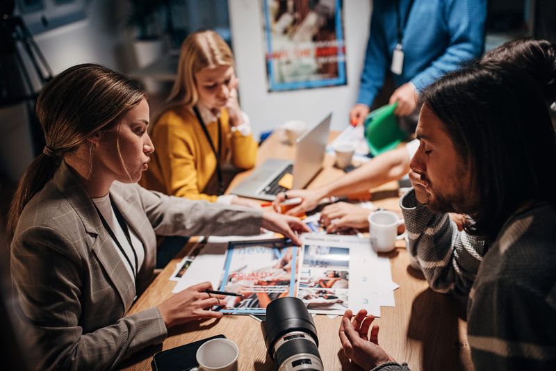 Group of people, male and female journalists working together on a board meeting in news editorial office at night.