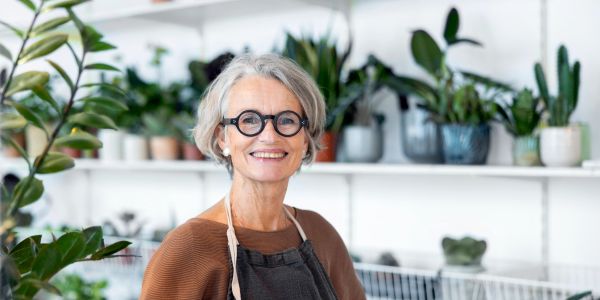 Smiling elderly woman in glasses and apron in a plant shop.