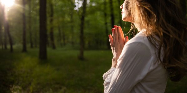 Woman praying with hands together in a forest.