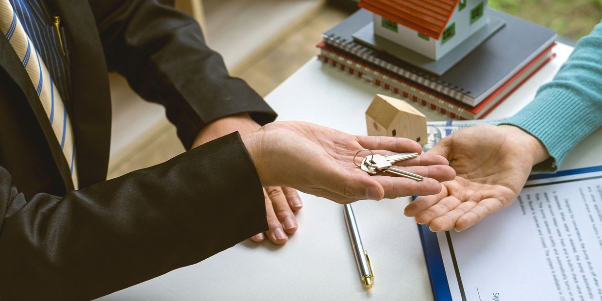 Person in suit handing over house keys to another person.