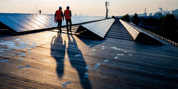 Two workers in safety vests inspect rooftop solar panels at sunset.