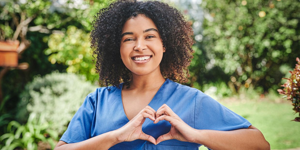 Smiling African American caregiver forming a heart shape to show compassion and support.