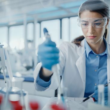 Scientist in a lab using a pipette with protective goggles and gloves.