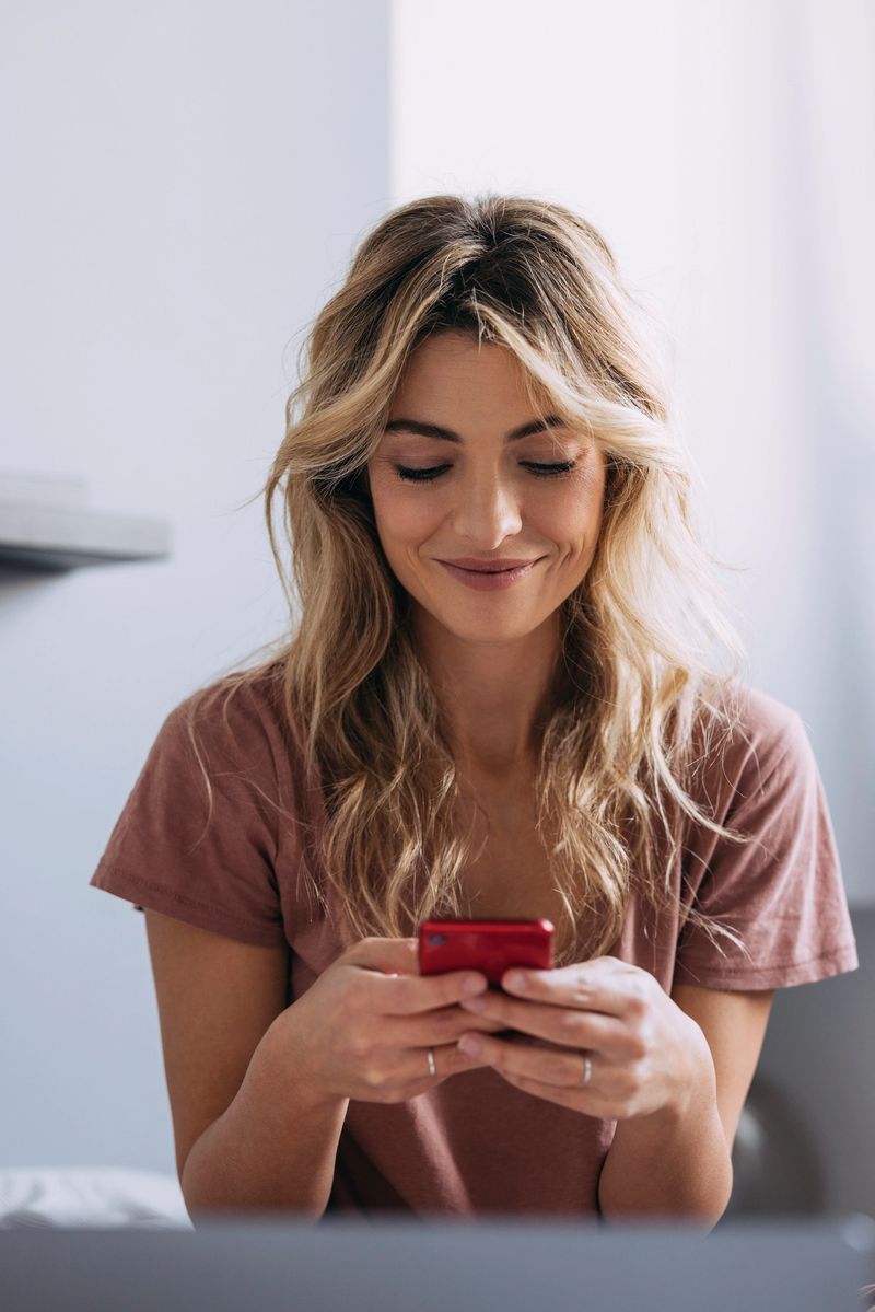 A beautiful female surfing the Internet on her new red phone, being happy and satisfied.