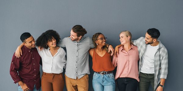 Six diverse friends standing arm-in-arm, smiling and enjoying each other's company.