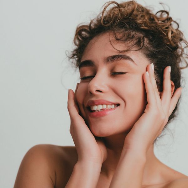 Young woman smiling with eyes closed, hands on face.