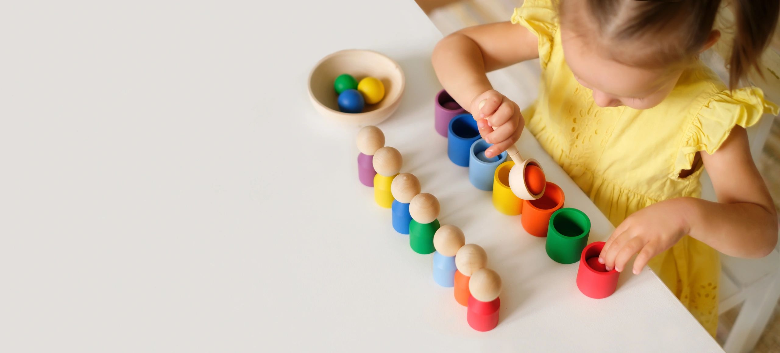 Child playing with colorful wooden toys at a white table.