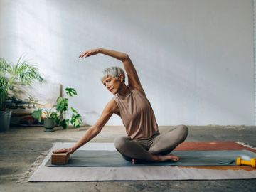 Older woman practicing the balasana yoga stretch on a mat indoors.