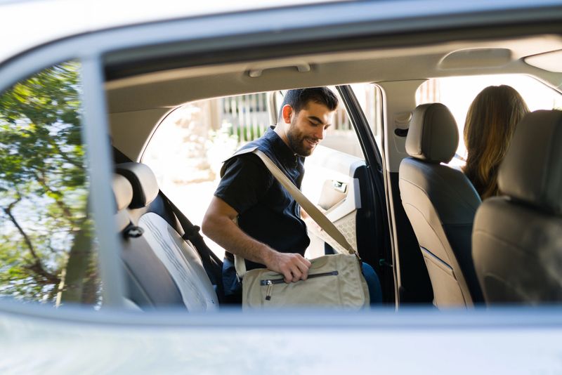 Handsome male passenger smiling and getting on a rideshare car while talking to the female driver