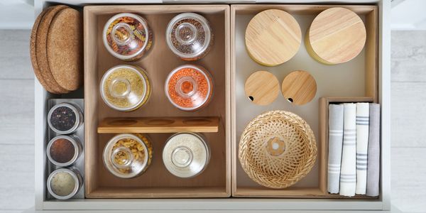 Organized kitchen drawer with jars, baskets, and cloths.