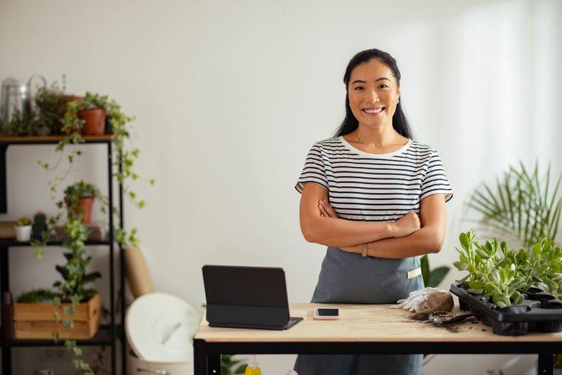 Cheerful smiling Asian woman standing at her plant shop with crossed arms and looking at camera.