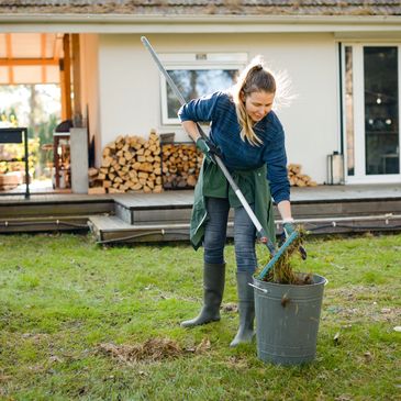 Woman cleaning grass debris into a bucket in the yard.