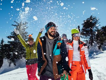 Group of friends enjoying a playful snowball fight in colorful winter attire.