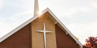 Sunlit church roof with white cross and steeple.