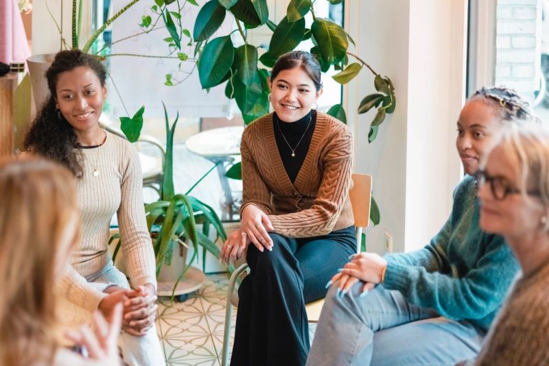 Multi-ethnic group of women sitting in a group therapy session. Group of women sitting in a circle on group therapy looking at their therapist and listening to her story.